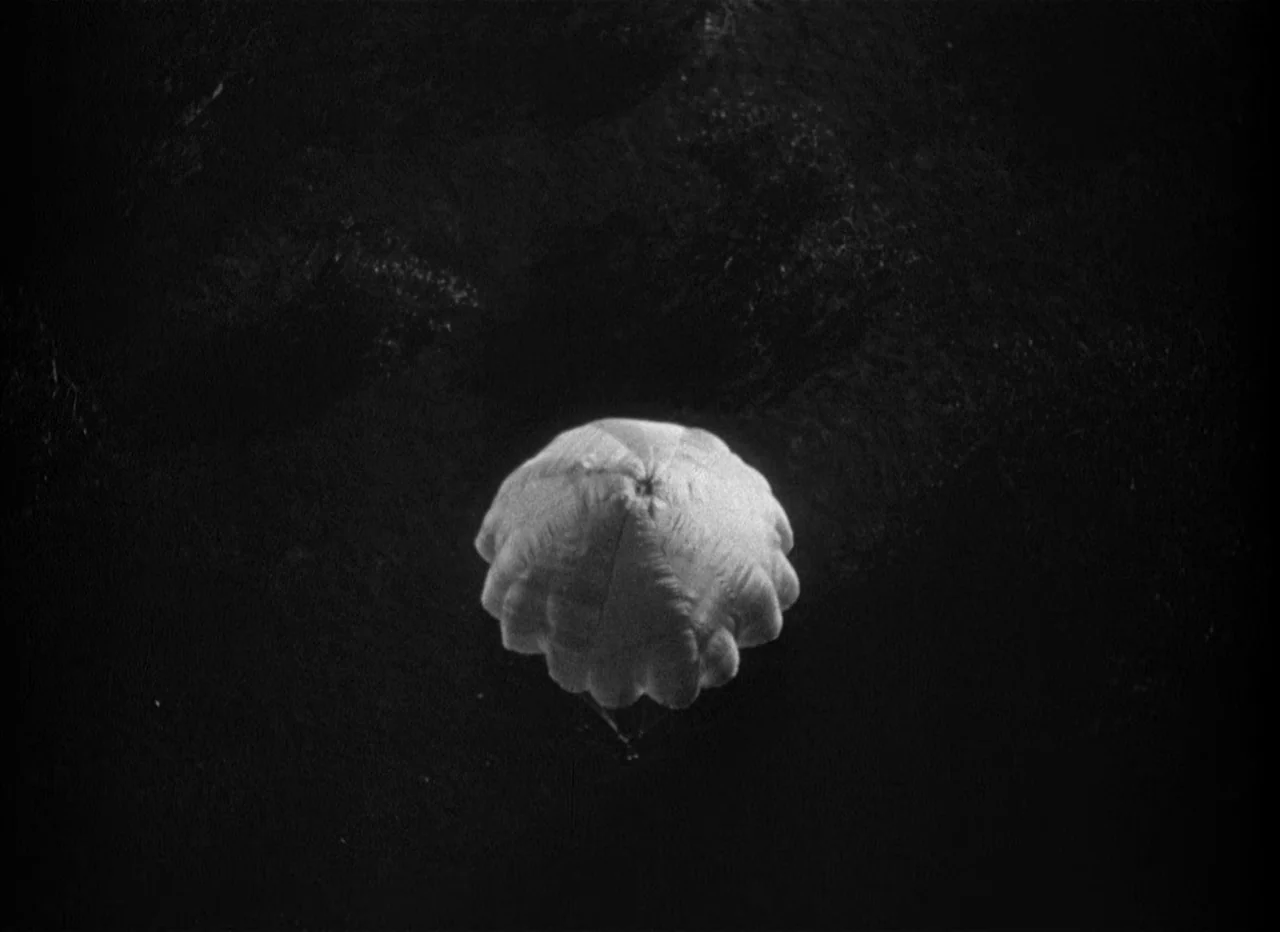 Dead Reckoning (1946) movie still: wide — A dark night scene shows a single white parachute floating above black water. The parachute is the only…