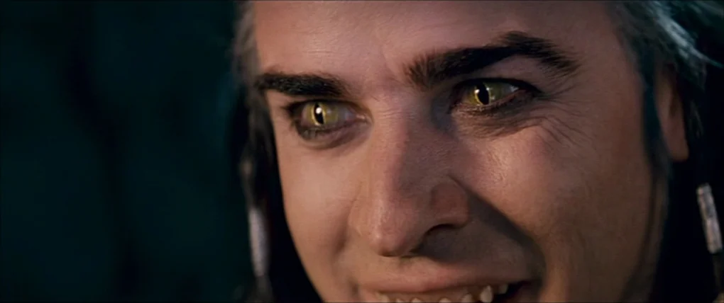 Your Highness (2011) movie still: closeup — A man with reptilian eyes sits in a dark, indistinct interior setting. He wears headphones and gazes…