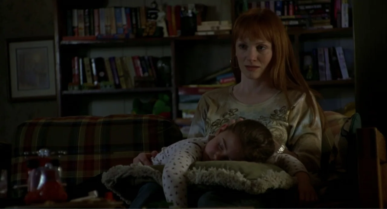 Ladder 49 (2004) movie still: medium — A dimly lit room features a bookshelf filled with books behind a seated woman. A woman holds a sleeping child…
