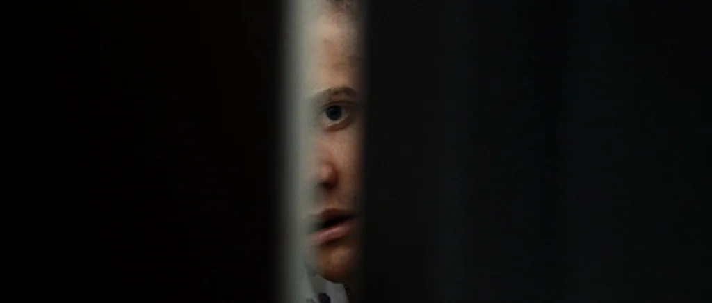 Jarhead movie still: closeup — A dark space defined by two large vertical black forms creating a narrow gap. A person's partial face is visible…