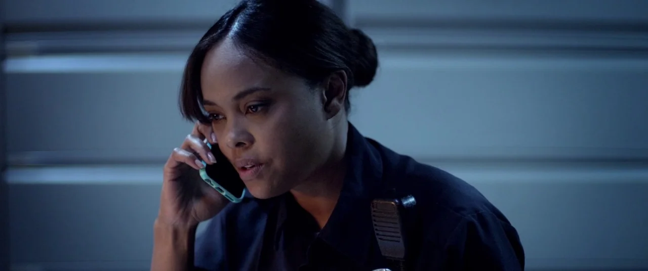 Blindfire (2020) movie still: closeup — A woman in a police uniform sits inside a vehicle at night. She holds a smartphone to her ear while speaking.