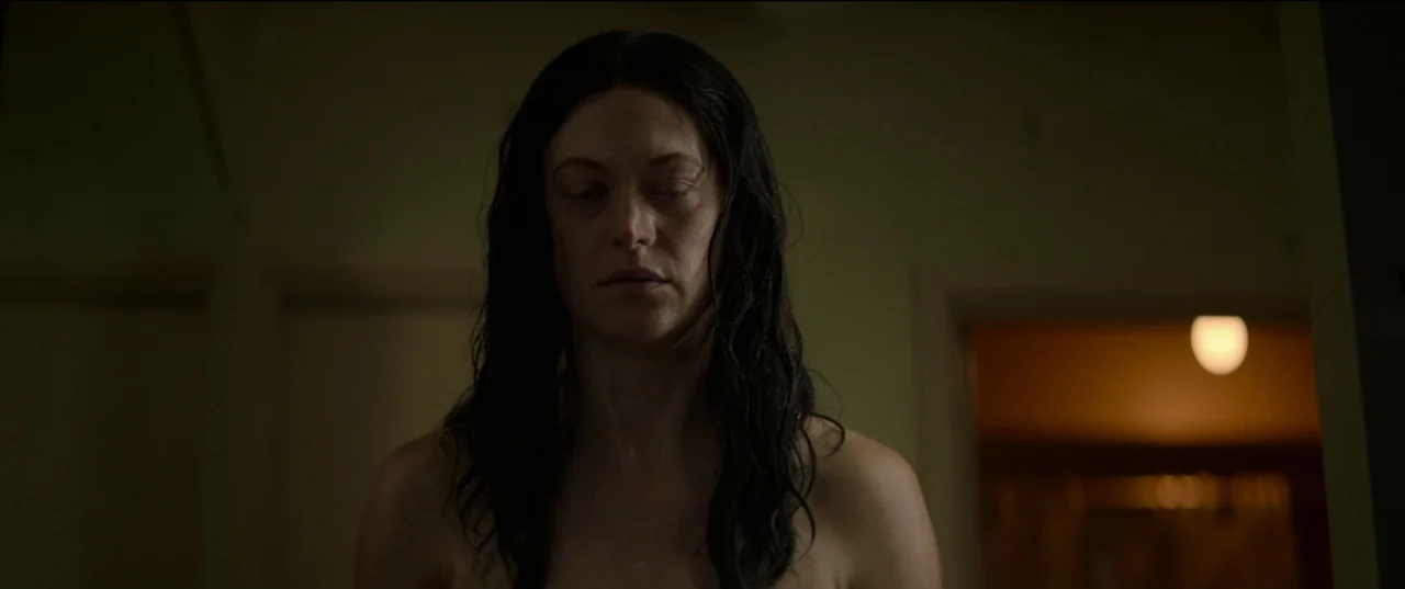 Birth/Rebirth (2023) movie still: medium — A dimly lit room with a subject in the foreground and a blurred doorway. A woman with wet, dark hair…