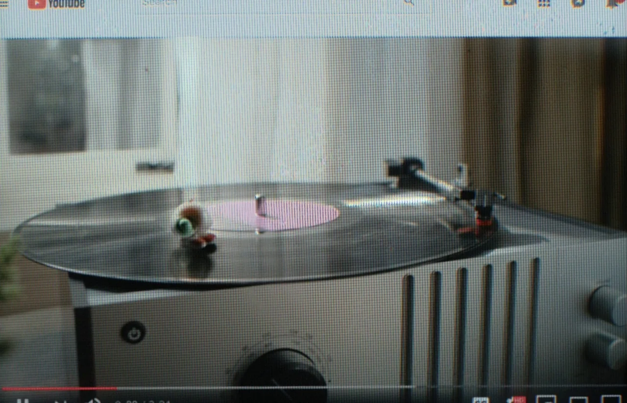 Marcel the Shell with Shoes On (2021) movie still: closeup — A silver record player sits on a surface with a soft-focus background behind it. A…