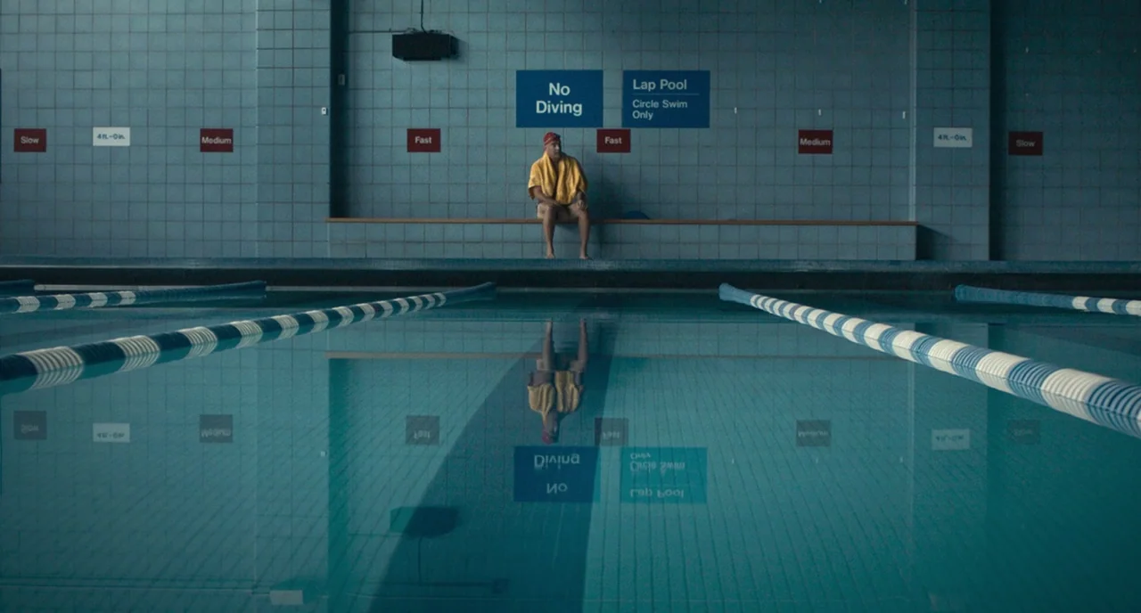 A Beautiful Day In The Neighborhood movie still: wide — An indoor swimming pool with blue tiled walls and lane markers reflecting on the surface. A…