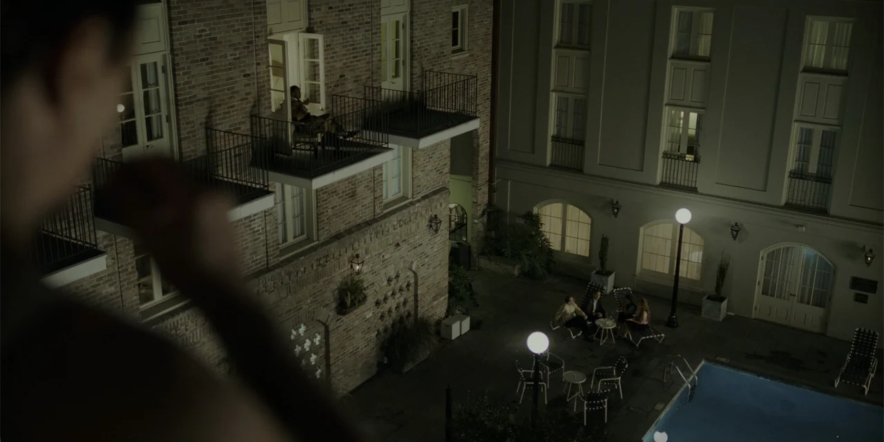 Green Book (2018) movie still: wide — A brick hotel building features balconies overlooking a ground-level courtyard with a pool. A small group of…