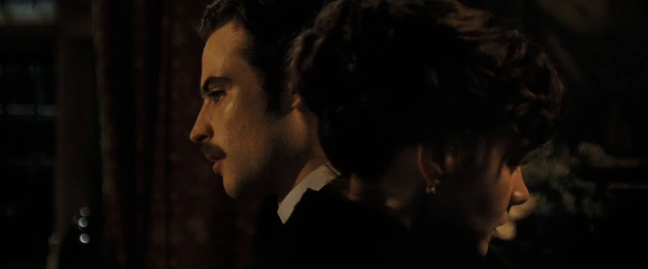 Far from the Madding Crowd (2015) movie still: medium — A dark, dimly lit indoor space features two people positioned closely back to back. The man…