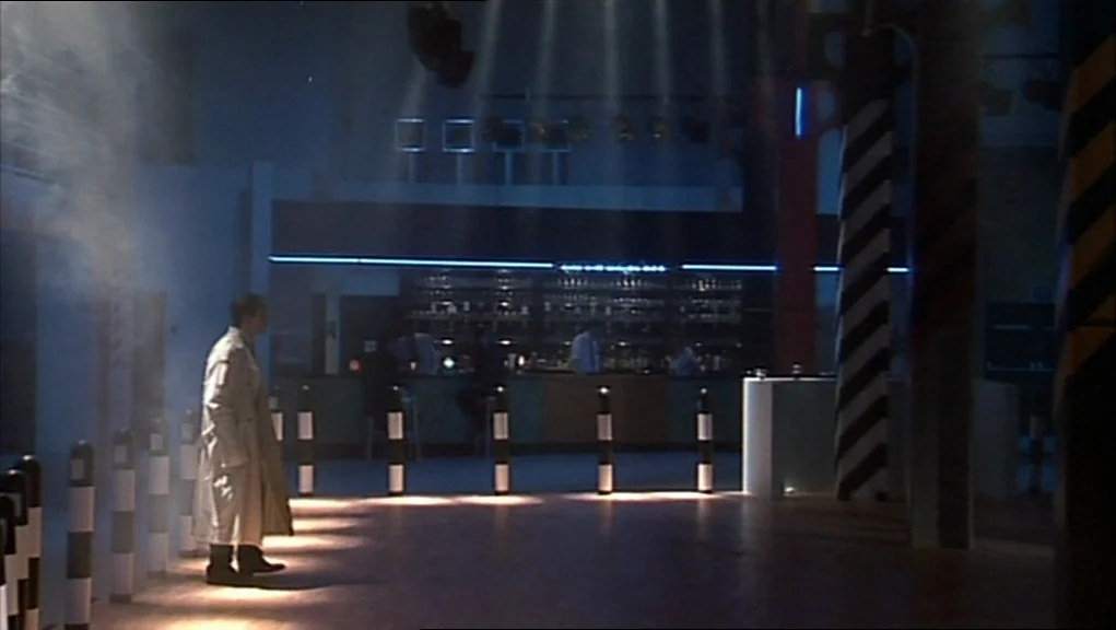24 Hour Party People movie still: wide — A spacious nightclub interior features black and white striped columns and a distant bar. A lone man in a…