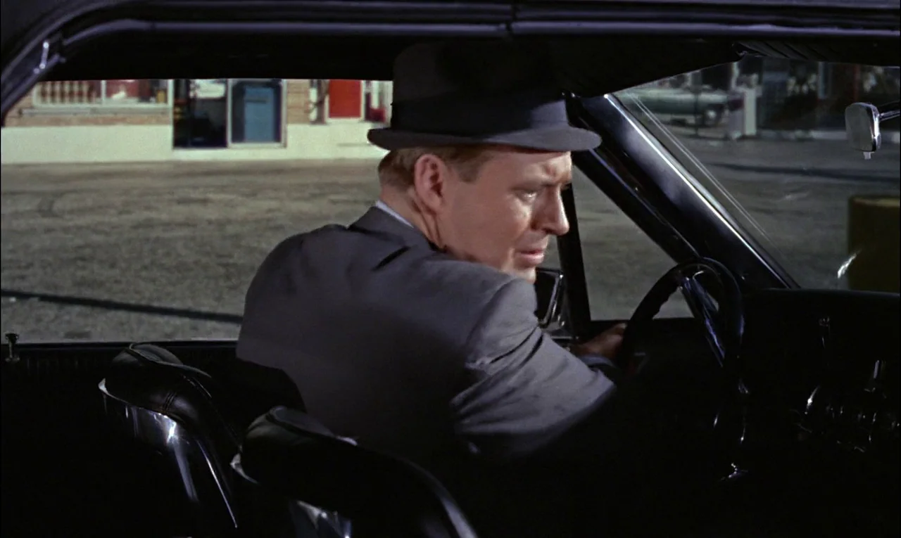 Goldfinger (1964) movie still: medium — A man sits behind the steering wheel of a vehicle at night. He turns his head to look out the passenger side…