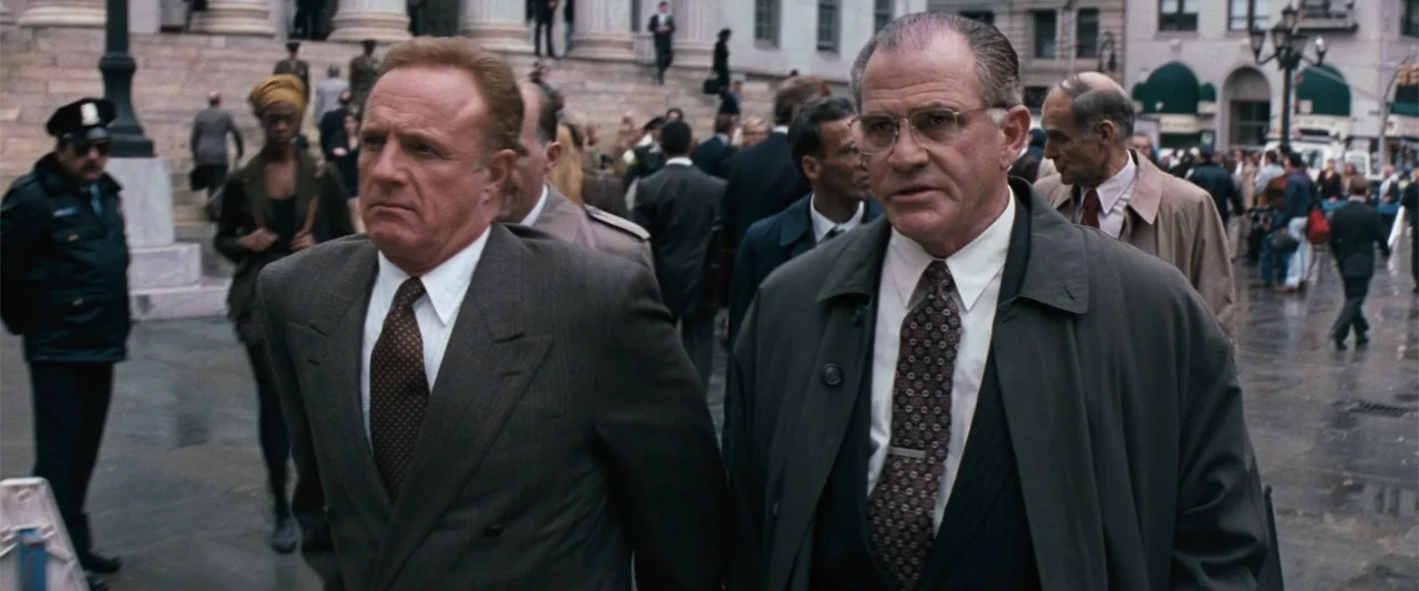 The Eraser (1977) movie still: medium — Two men walk past a grand stone courthouse with columns in a busy plaza. They are dressed in formal business…