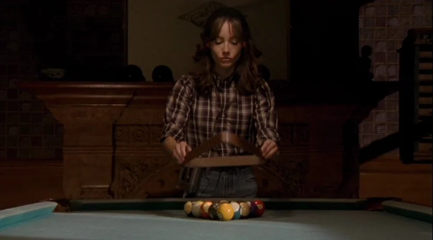 The House Of The Devil (2009) movie still: medium — A dimly lit room features a pool table with a rack of billiard balls. A young woman stands…