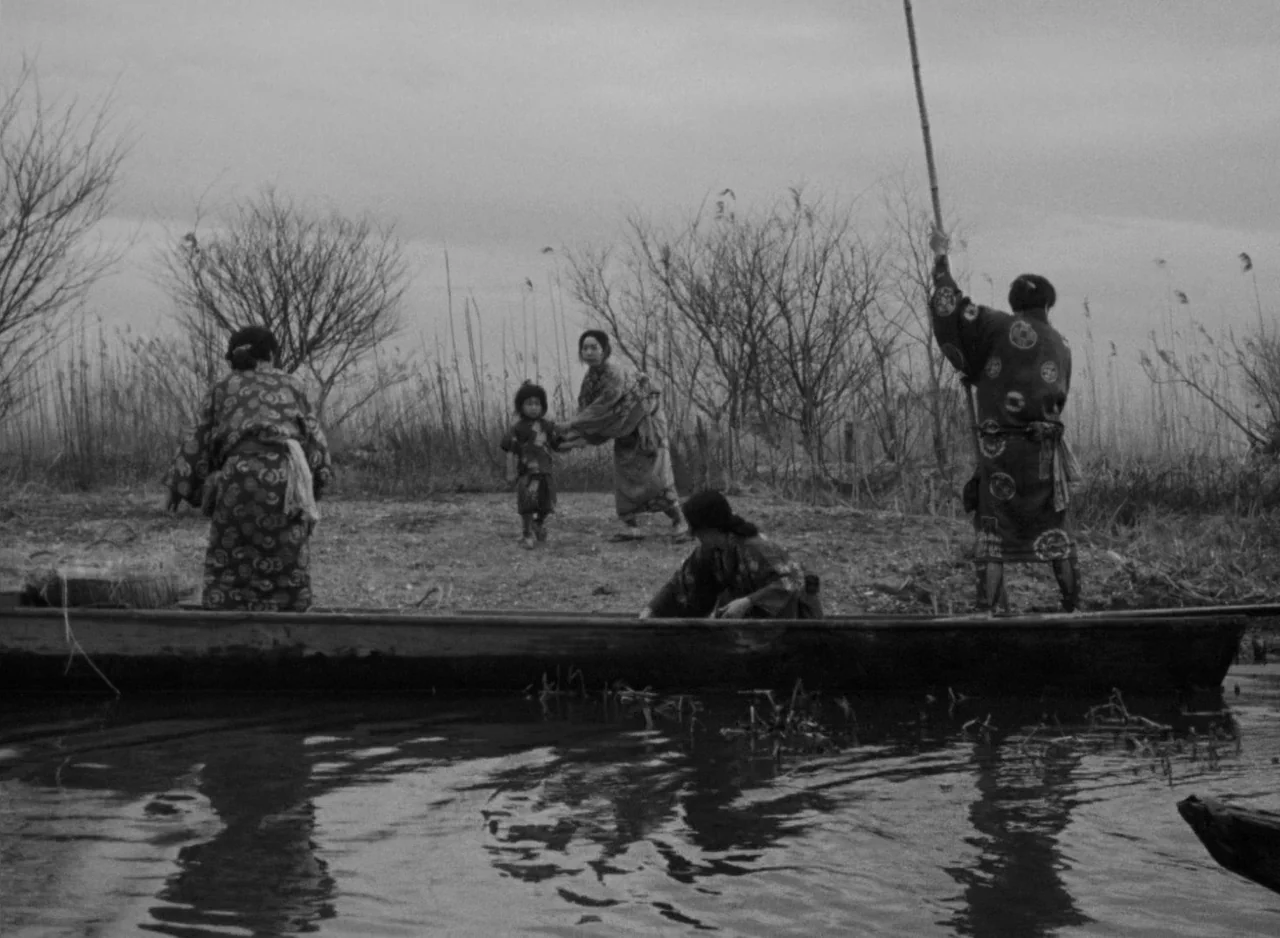 Ugetsu (1953) movie still: wide — A flat marshland area with sparse, leafless trees under a cloudy sky. A wooden boat rests at the edge of the water…