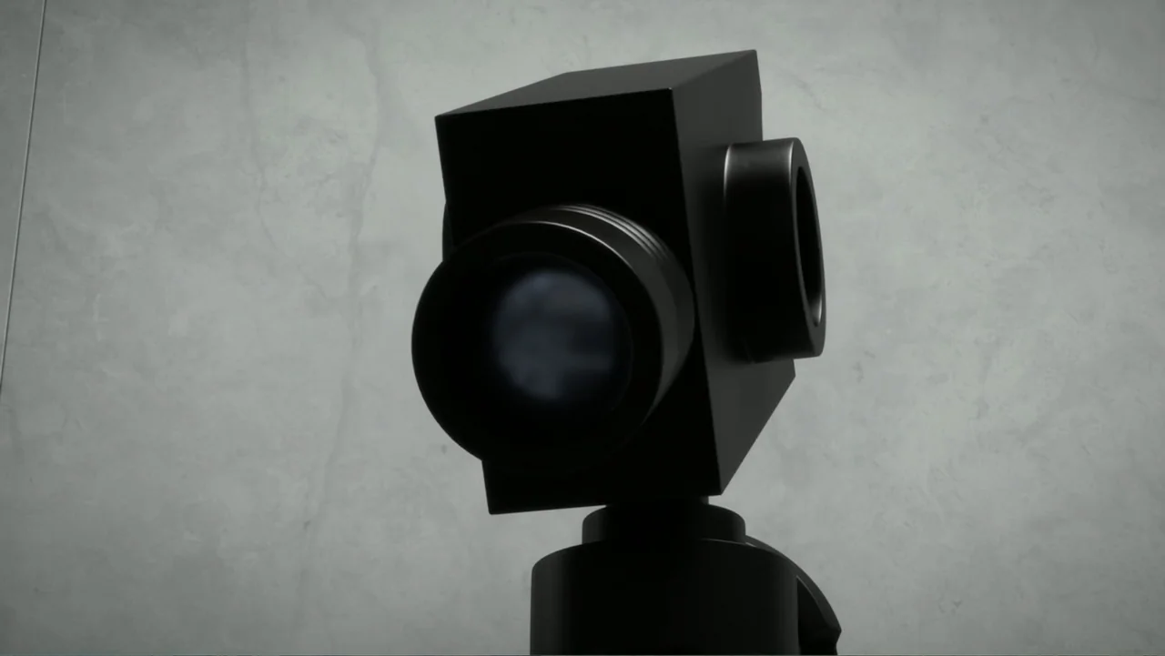 LEGO DC Batman: Family Matters (2019) movie still: closeup — A close-up view of a black camera body against a plain gray wall. The lens faces…