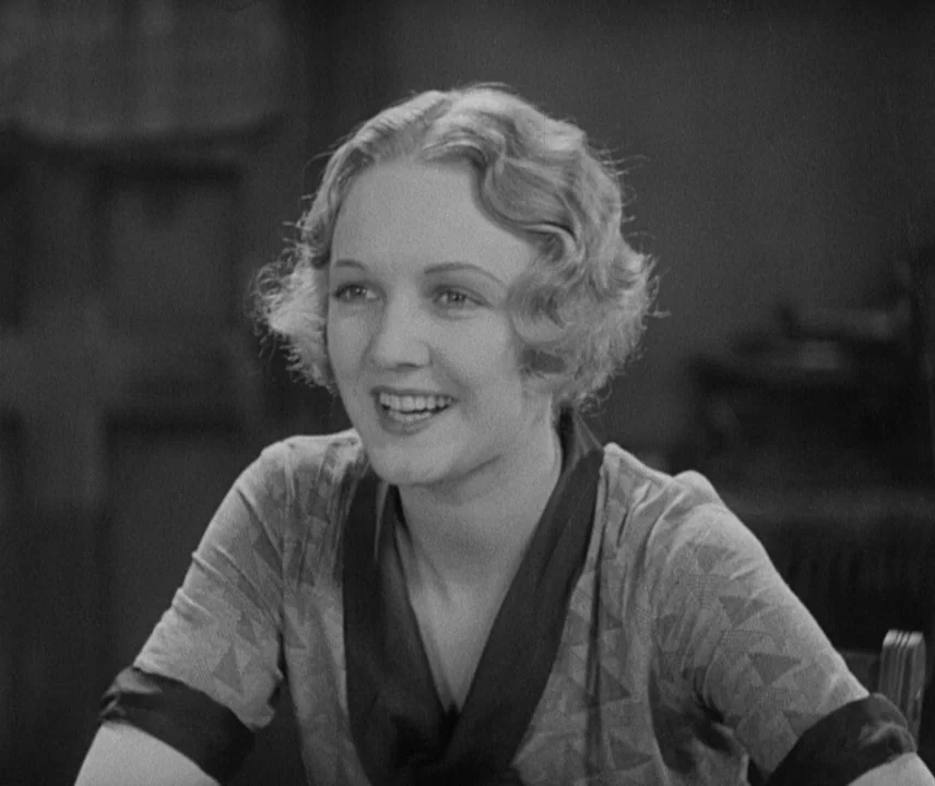City Lights (1931) movie still: medium — A woman sits indoors against a simple, dark blurred backdrop. She looks off-camera to the side while smiling.