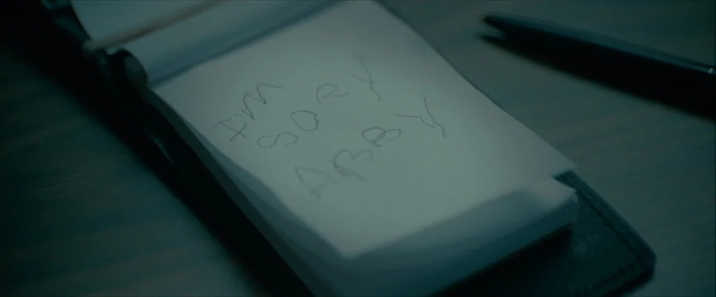 Let Me In (2010) movie still: closeup — A close-up of a notepad resting on a dark desk surface. The handwritten message on the paper reads I'M SORY…