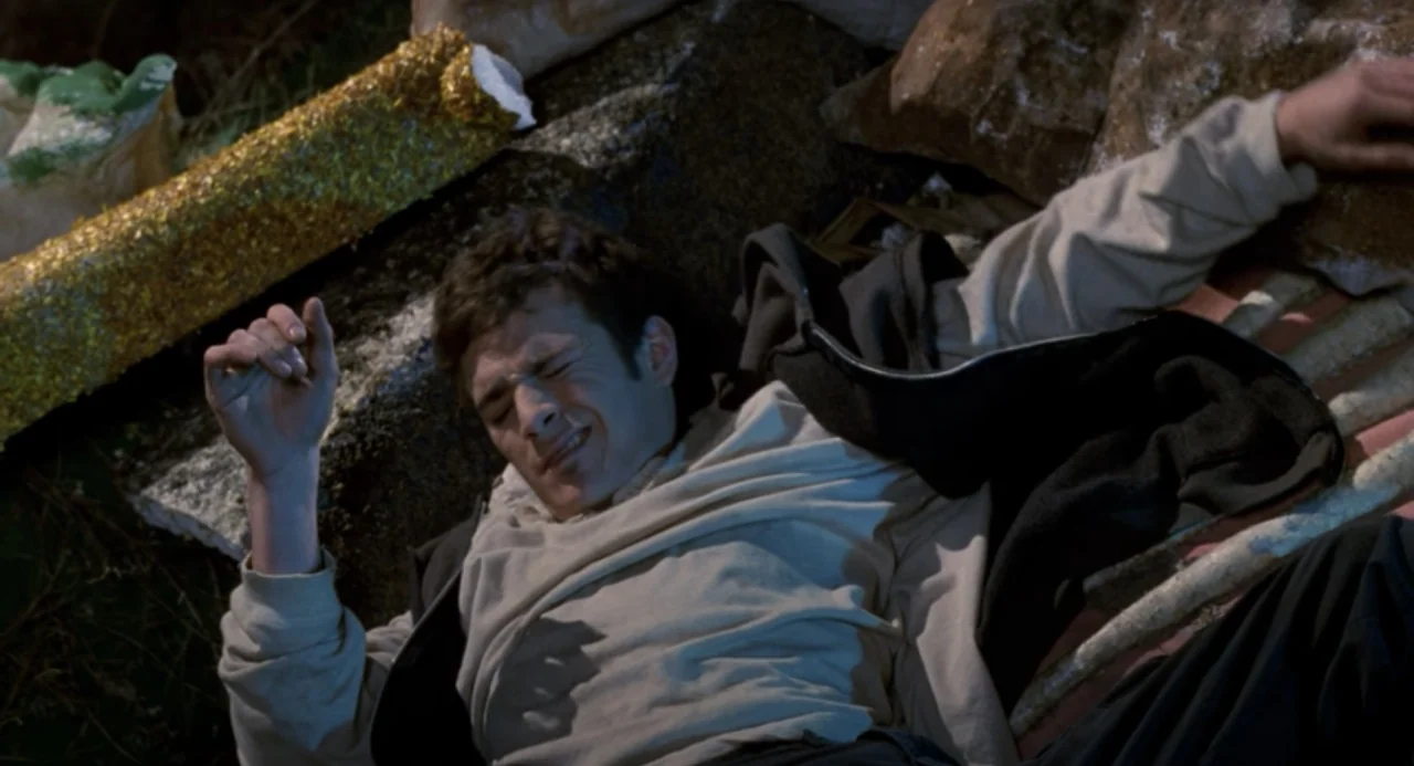 Buffy the Vampire Slayer (1992) movie still: medium — A man lies on his back amidst scattered dark rocks and debris. He wears a layered top and…