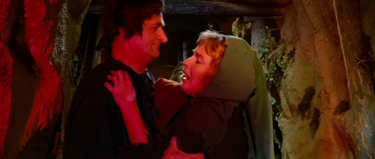 Night of the Blood Monster (1970) movie still: medium — An interior cave setting with rough, earthy rock walls and dim, shadowed recesses. A woman…