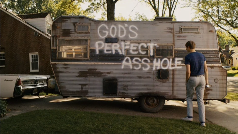 Youth In Revolt (2009) movie still: fullbody — A suburban street scene features a weathered vintage trailer parked on a concrete driveway. The side…