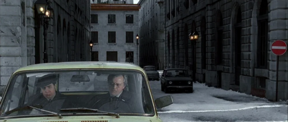 Confessions of a Dangerous Mind (2002) movie still: wide — A quiet urban street is lined with stone buildings and covered in light snow. Two men sit…