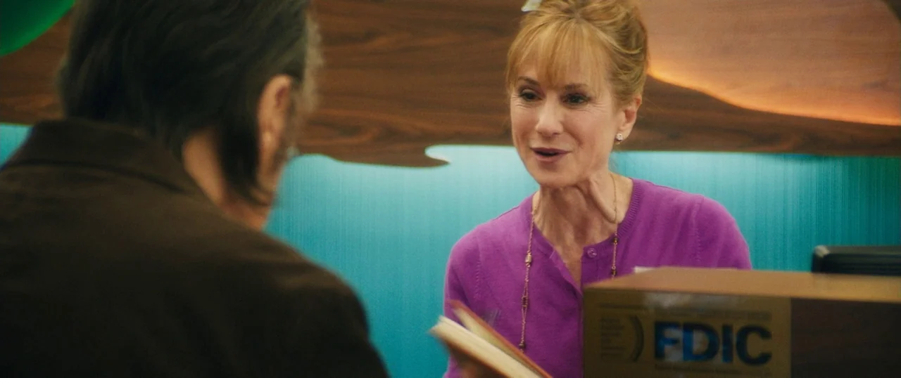 Manglehorn (2014) movie still: medium — A woman stands behind a counter with a blue wall and a wooden fixture. She speaks to an unseen individual…