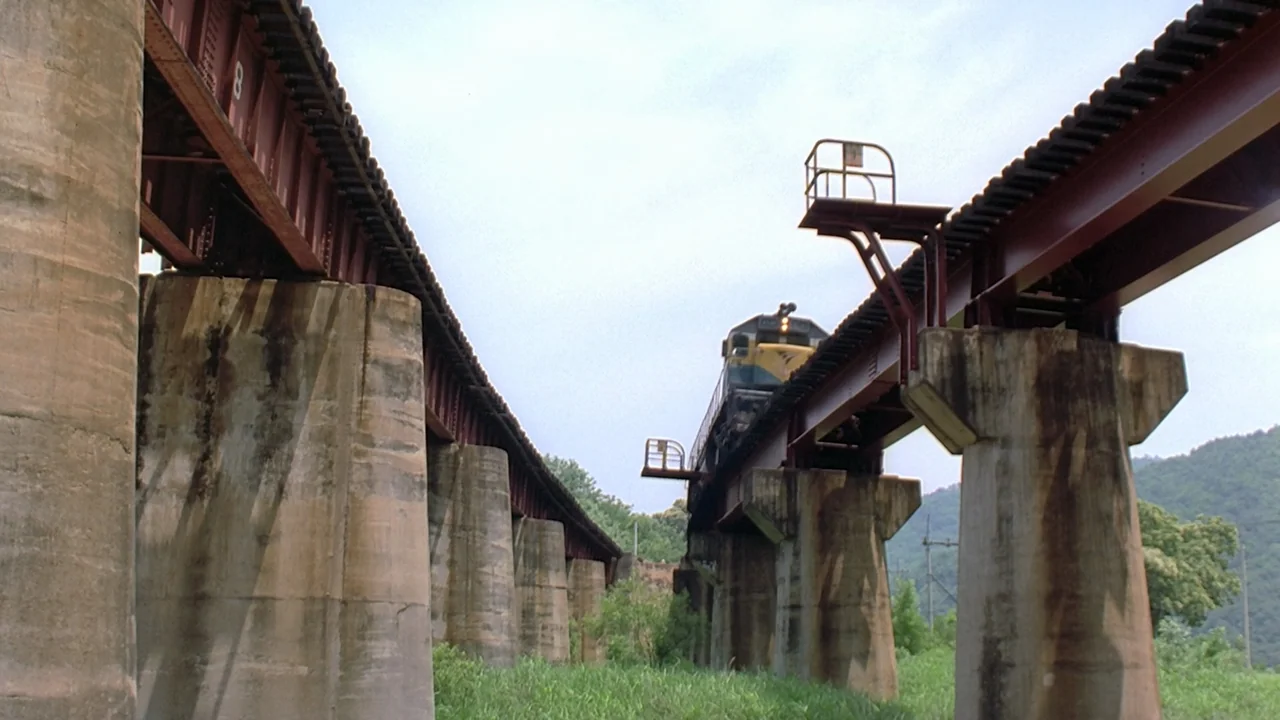 Peppermint Candy (1999) movie still: wide — Two parallel railway bridges constructed of steel beams and concrete pillars cross open countryside. A…