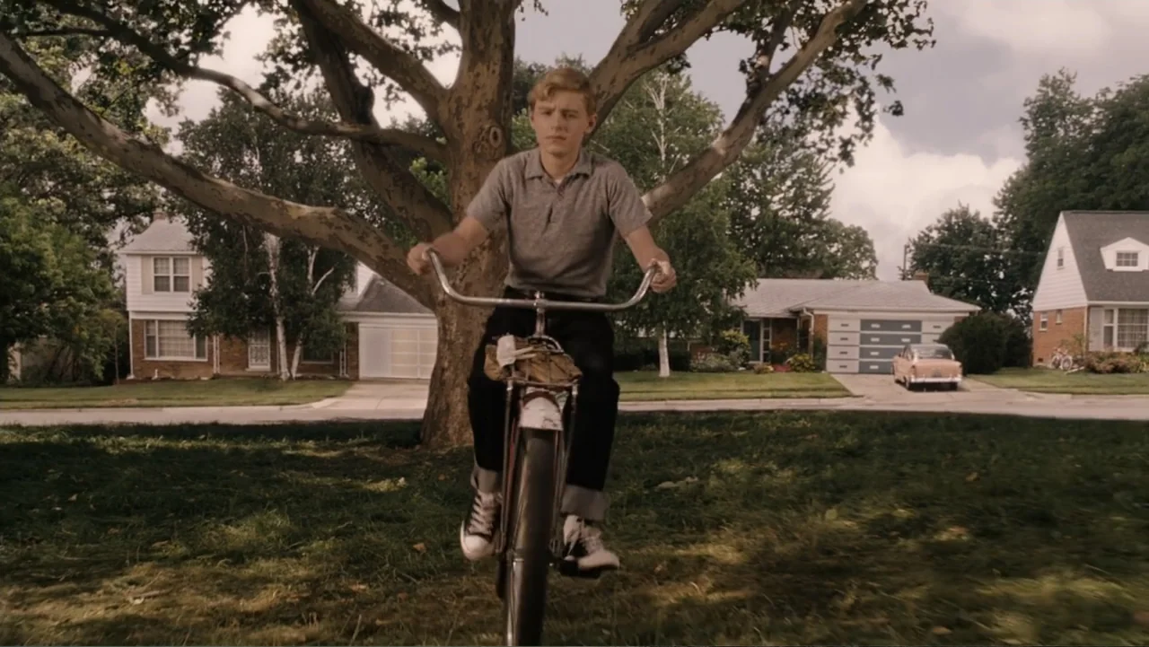 Flipped (2010) movie still: medium — A suburban front yard features a large deciduous tree and residential houses in the background. A teenage boy…