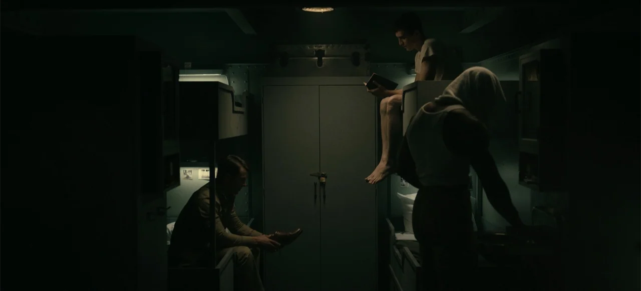 Devotion (2022) movie still: medium — A cramped military-style bunk area features metallic lockers and stacked sleeping berths. Three men occupy the…