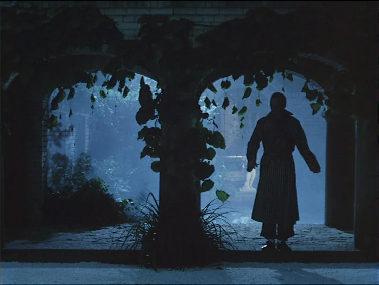 All These Women (1964) movie still: fullbody — A dark stone courtyard at night features double arches covered in creeping green vines. A lone man in…