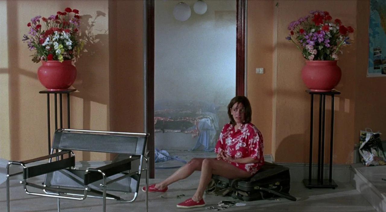 Women on the Verge of a Nervous Breakdown (1988) movie still: medium — A peach-walled interior space features two symmetrical red planters filled…