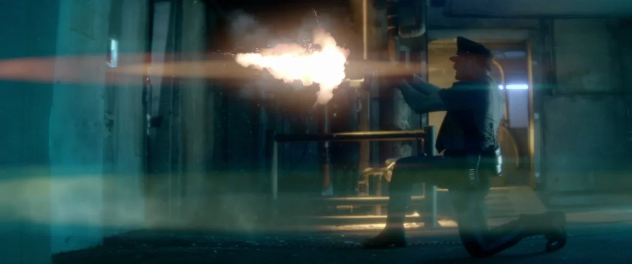 Officer Downe (2016) movie still: fullbody — A dimly lit parking garage structure with exposed concrete pillars and industrial piping. A uniformed…