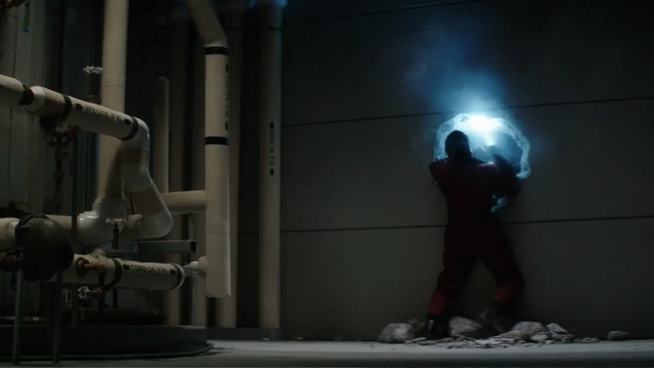 Skyscraper (2018) movie still: fullbody — A dimly lit industrial room contains large white pipes and a grey concrete wall. A person in a red…