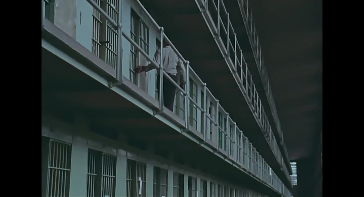 Free Chol Soo Lee (2022) movie still: wide — A multi-tiered prison wing features long metal walkways and rows of barred doors. A man walks along the…