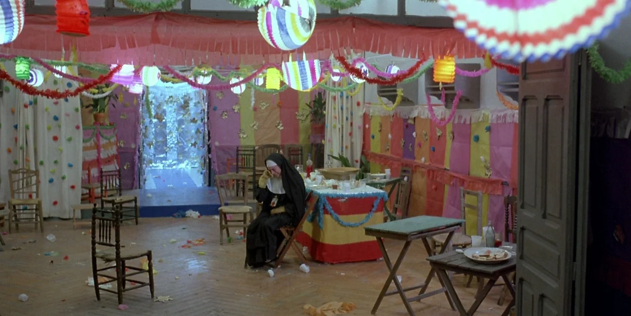 Dark Habits (1983) movie still: wide — A room decorated for a celebration with colorful paper streamers and paper lanterns hangs overhead. A single…