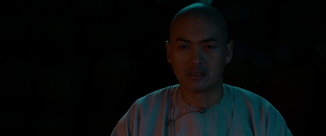 Crouching Tiger, Hidden Dragon (2000) movie still: medium — A man stands centered in a dark, poorly lit environment with deep black surroundings. He…