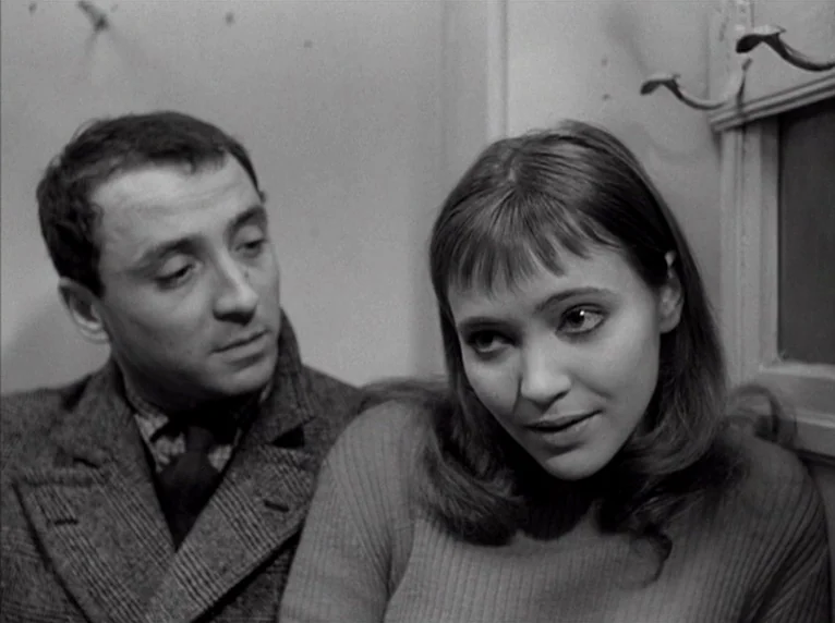 Band of Outsiders (Bande à part) (1964) movie still: medium — A man and woman are positioned close together against a plain wall. The woman looks…