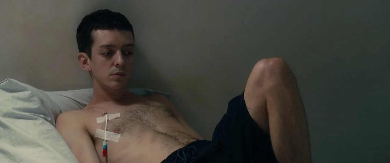 BPM (Beats Per Minute) (2017) movie still: medium — A plain room with light grey walls contains a single hospital bed. A shirtless man lies on the…