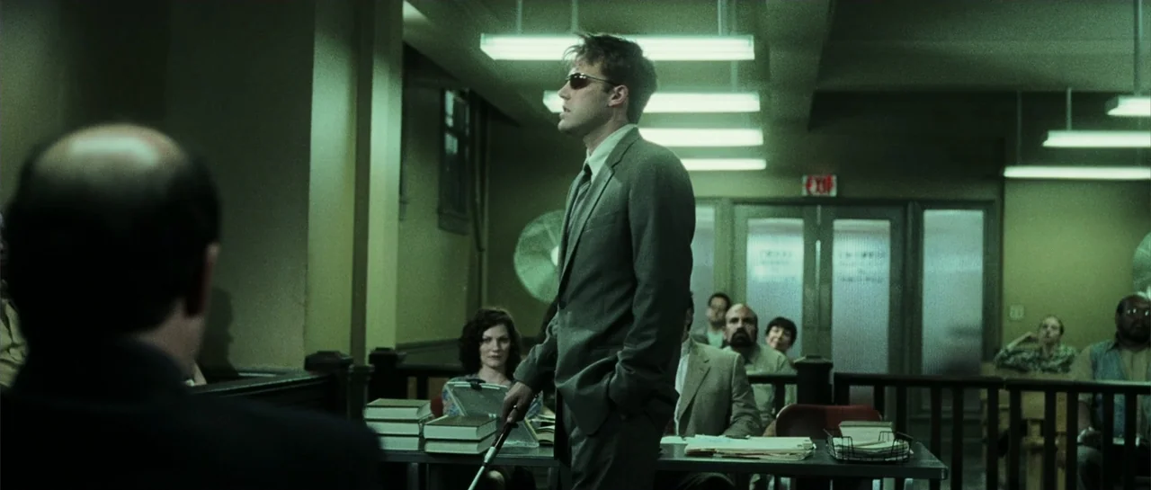 Daredevil (2015) movie still: medium — A drab office filled with desks and papers features greenish walls and fluorescent lights. A man in a suit…