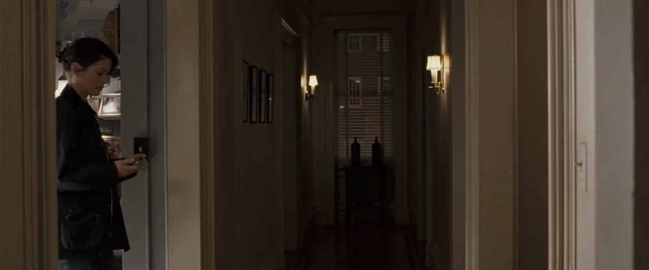 No Reservations (2007) movie still: medium — A residential hallway at night features wooden floors and muted cream-colored walls. A woman stands in…