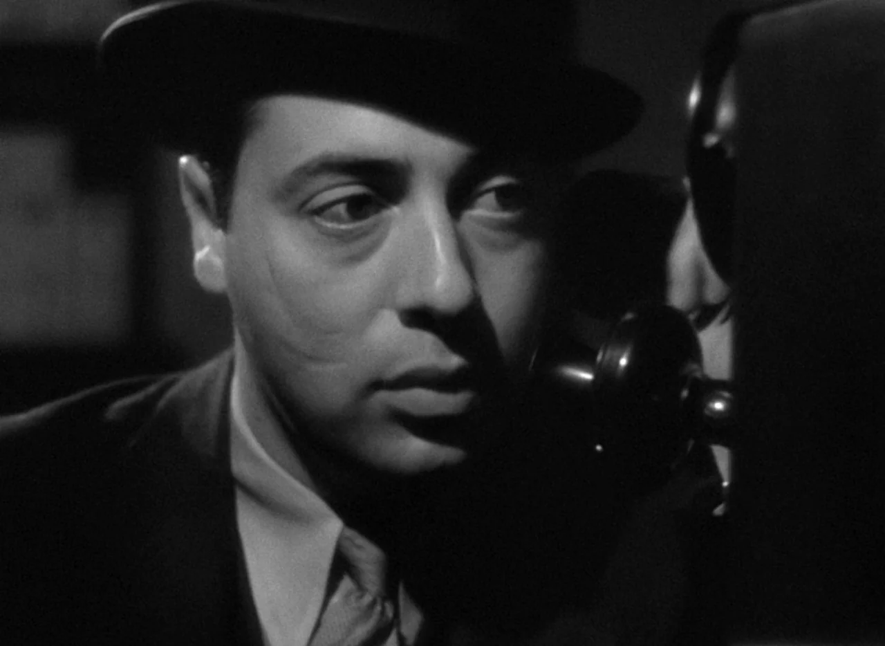 The Thin Man (1934) movie still: closeup — A dimly lit interior setting with high contrast lighting typical of 1940s noir film. A man in a dark…