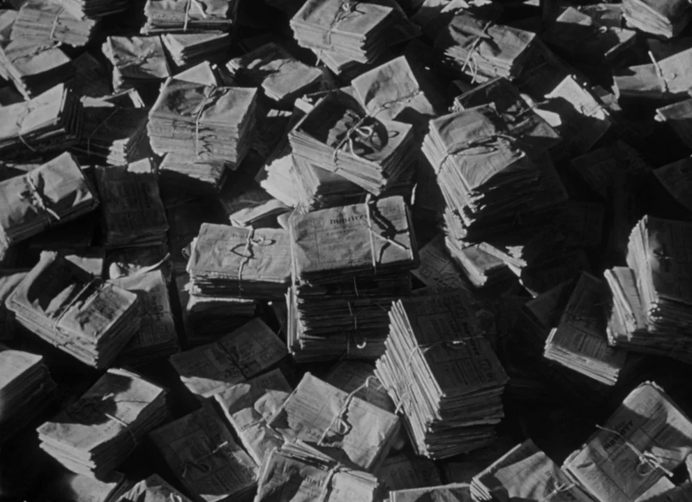Citizen Kane (1941) movie still: establishing — A dense pile of weathered paper stacks tied with string rests on a floor. Each bundle contains…
