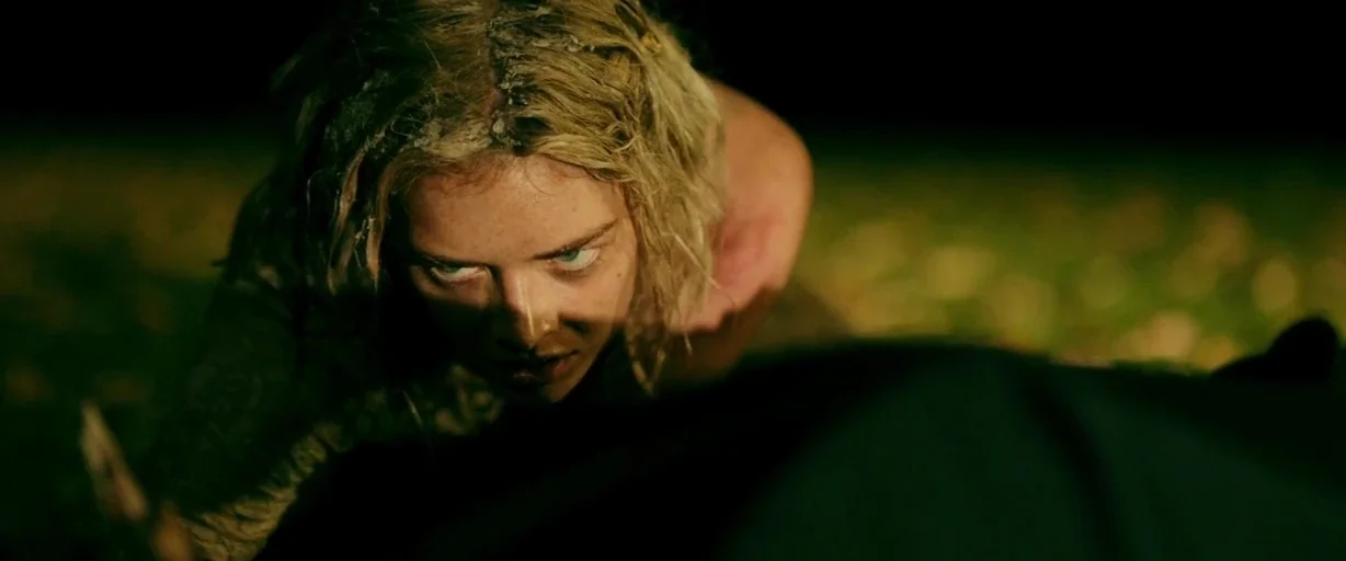 Ready or Not (2019) movie still: closeup — A night setting in a grassy field with low, ground-level visibility. A blonde woman crawls forward on the…