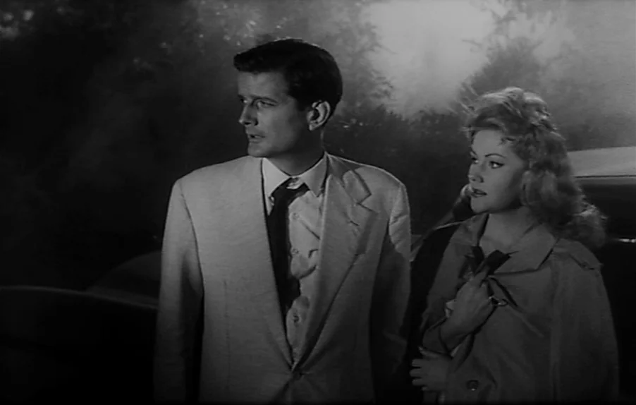 Caltiki, The Immortal Monster (1959) movie still: medium — A dark, misty roadside at night with trees visible in the soft-focus distance. A man and…