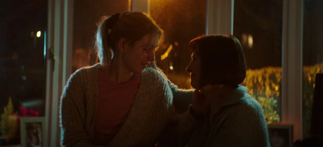 A Good Woman Is Hard To Find (2019) movie still: medium — A dark, dimly lit interior space with large glass windows showing a night exterior. One…