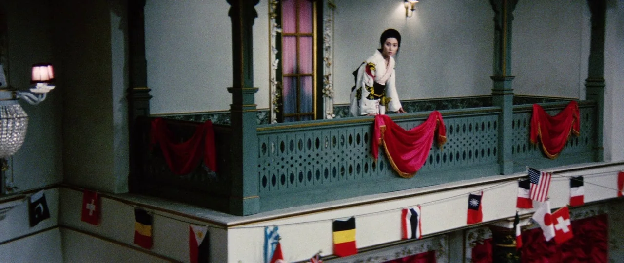 Lady Snowblood (1973) movie still: wide — A decorative interior balcony features green railings adorned with draped red fabric and flags. A woman in…