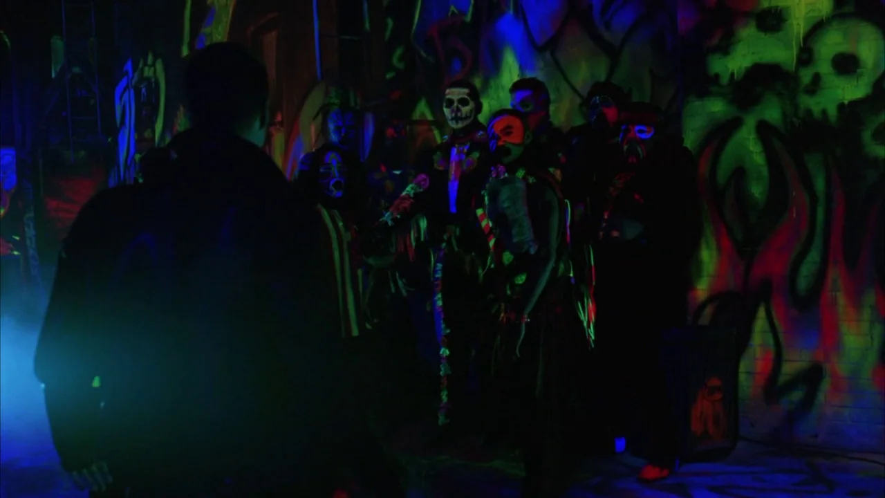Batman Forever (1995) movie still: medium — A dark brick alleyway is illuminated by vibrant neon blue and green graffiti artwork. A group of…
