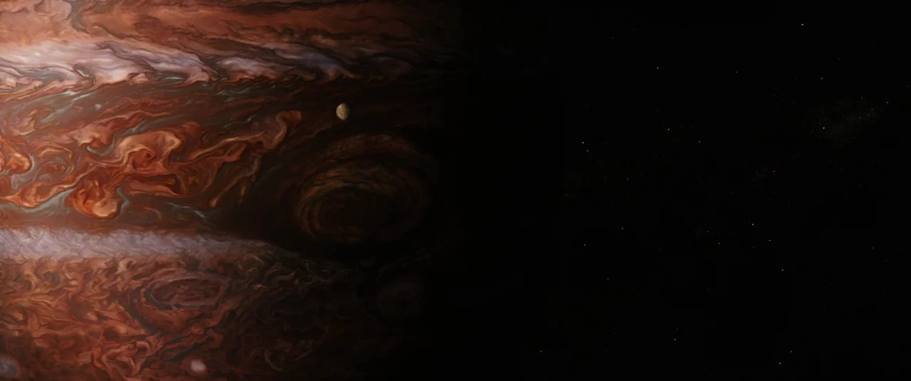 Jupiter Ascending (2015) movie still: establishing — A close-up view of the giant gas planet Jupiter dominates the left side. A small moon hangs in…