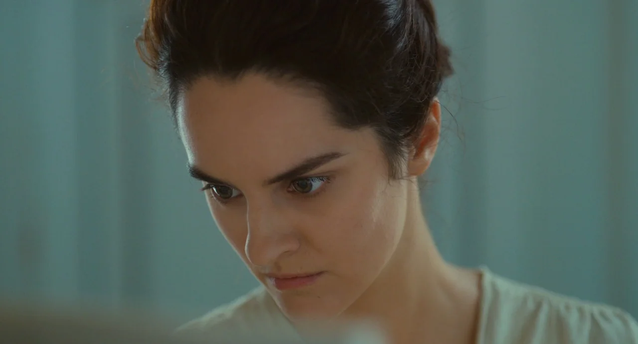 Portrait of a Lady on Fire movie still: closeup — A woman looks down with a concentrated expression in a minimalist indoor setting. The shot focuses…