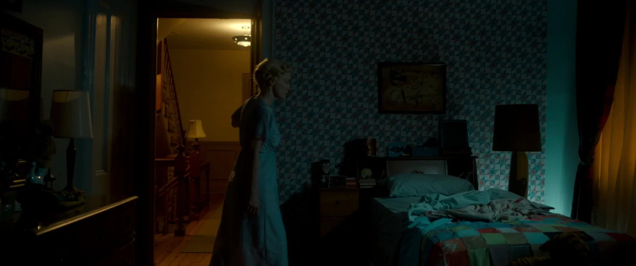 Mother’s Instinct (2024) movie still: medium — A dimly lit room features patterned wallpaper, a quilt-covered bed, and a wooden nightstand. A woman…