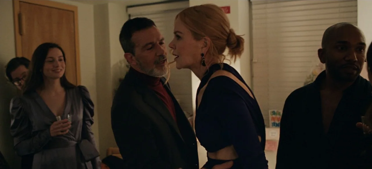 Babygirl (2024) movie still: medium — A well-lit residential interior space features several people gathered at a party. A middle-aged man and woman…