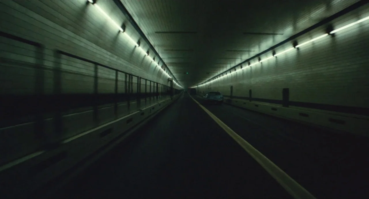 The Rain People (1969) movie still: establishing — A long, curved road tunnel constructed with white tiled walls and yellow road markings. A single…