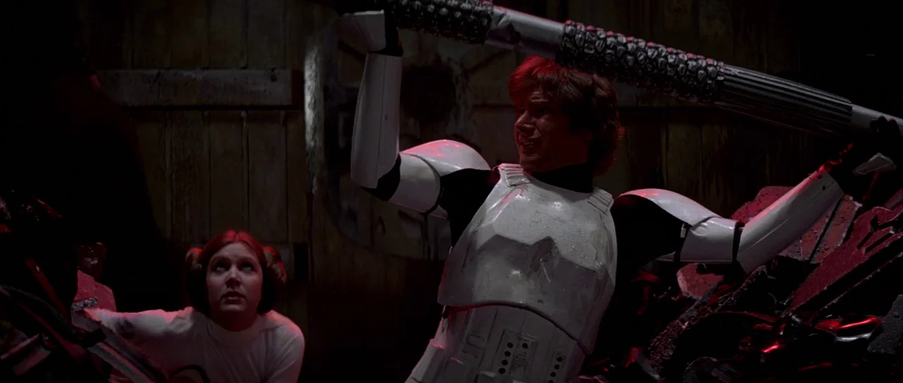 Star Wars (1977) movie still: medium — A dark, cramped industrial space filled with crushed metal debris and shadows. A man in stormtrooper armor…